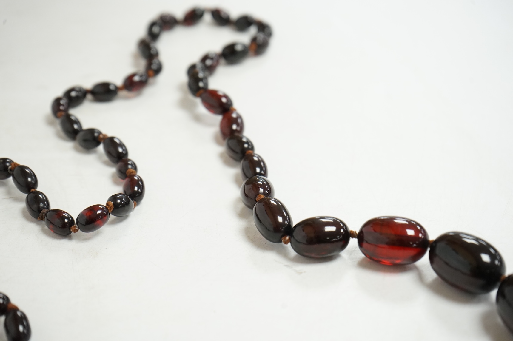 A single strand graduated simulated oval dark cherry amber bead necklace, 110cm, gross weight 90 grams.